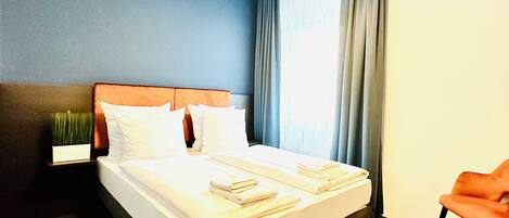 Ein Hotelzimmer mit Bett, Nachttisch, Stuhl und einem Fenster mit Vorhängen.