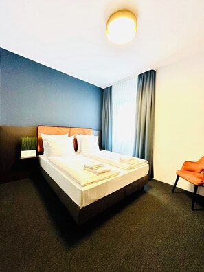 A hotel room with a bed, a nightstand, a chair, and a window with curtains. - Arthotel Ambassador Wiesbaden (Wiesbaden)