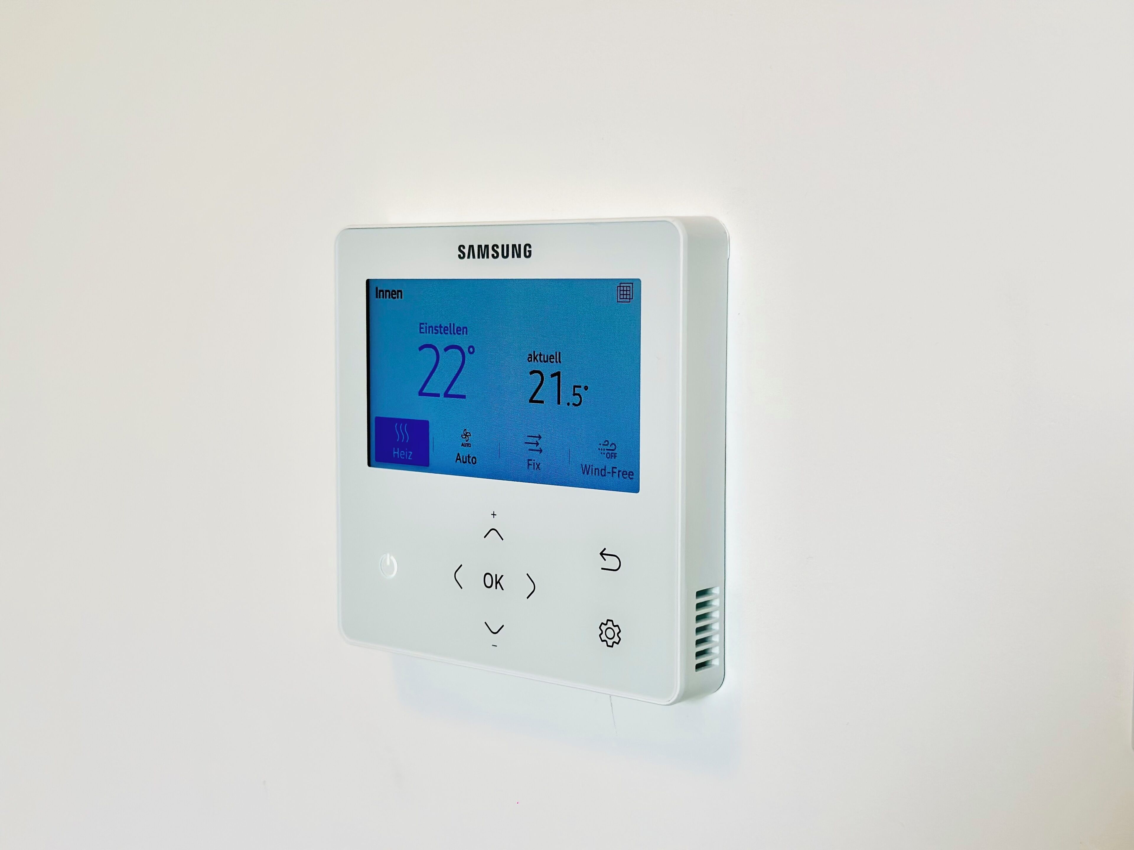 Un termostato inteligente Samsung con pantalla digital, ajustes de temperatura y botones de control.