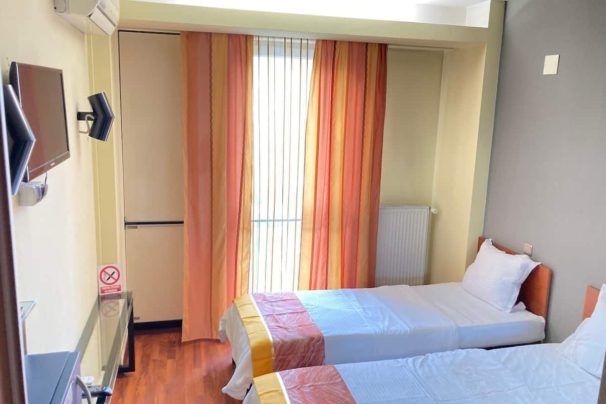Una habitación de hotel con dos camas, televisión, radiador y ventana con cortinas.
