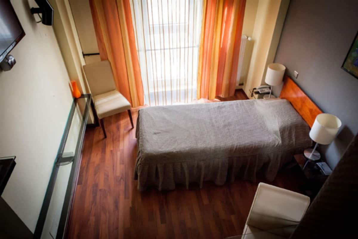 Una habitación de hotel con cama, una silla, un escritorio y una ventana con cortinas.