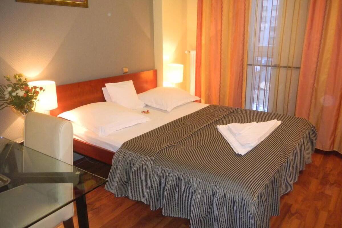 Una habitación de hotel con cama, escritorio y silla, y una ventana con cortinas.