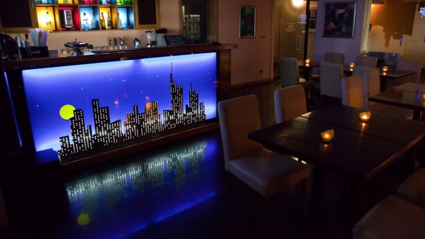 A bar area with a city skyline display, seating, and a variety of bottles on shelves. - Tania-Frankfurt (Bucharest)