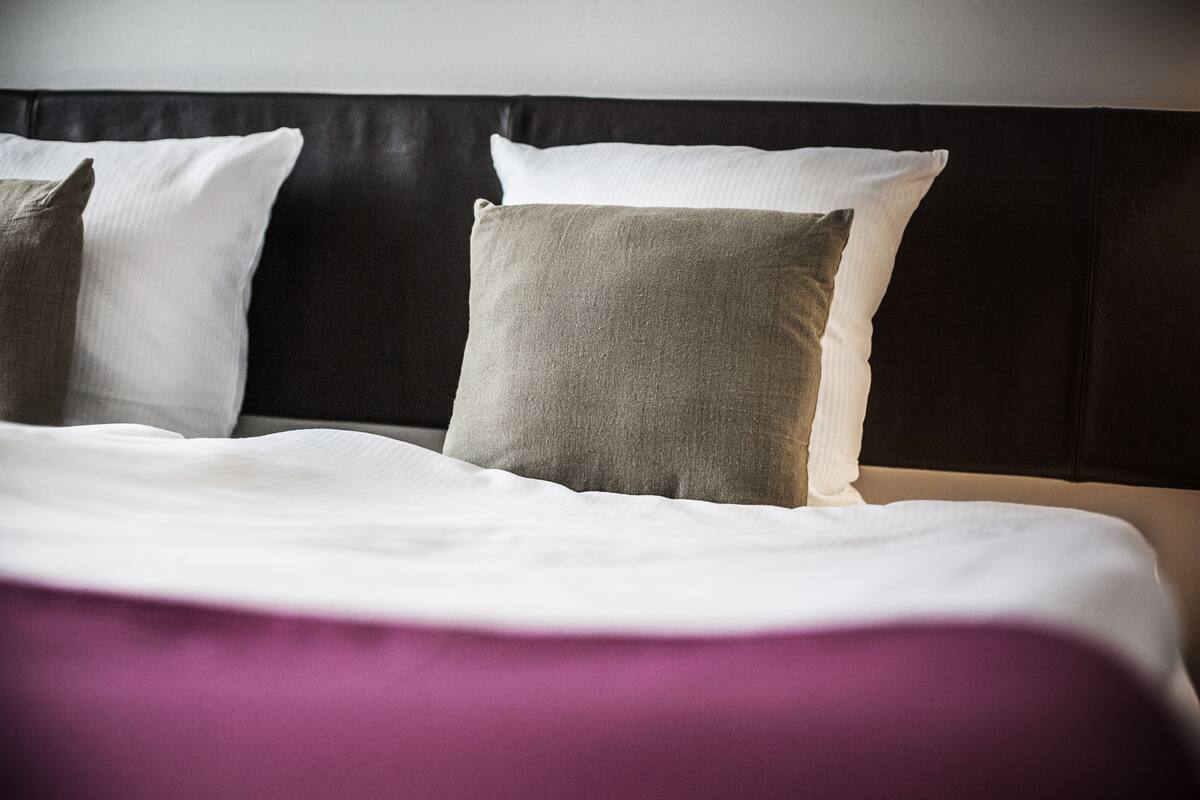 A bed with white and grey pillows, a black headboard, and a purple bedspread.