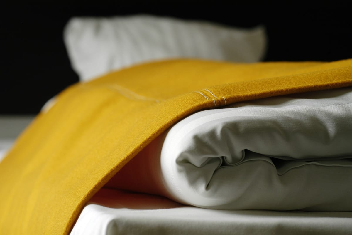 A neatly folded bed with a white and yellow blanket.