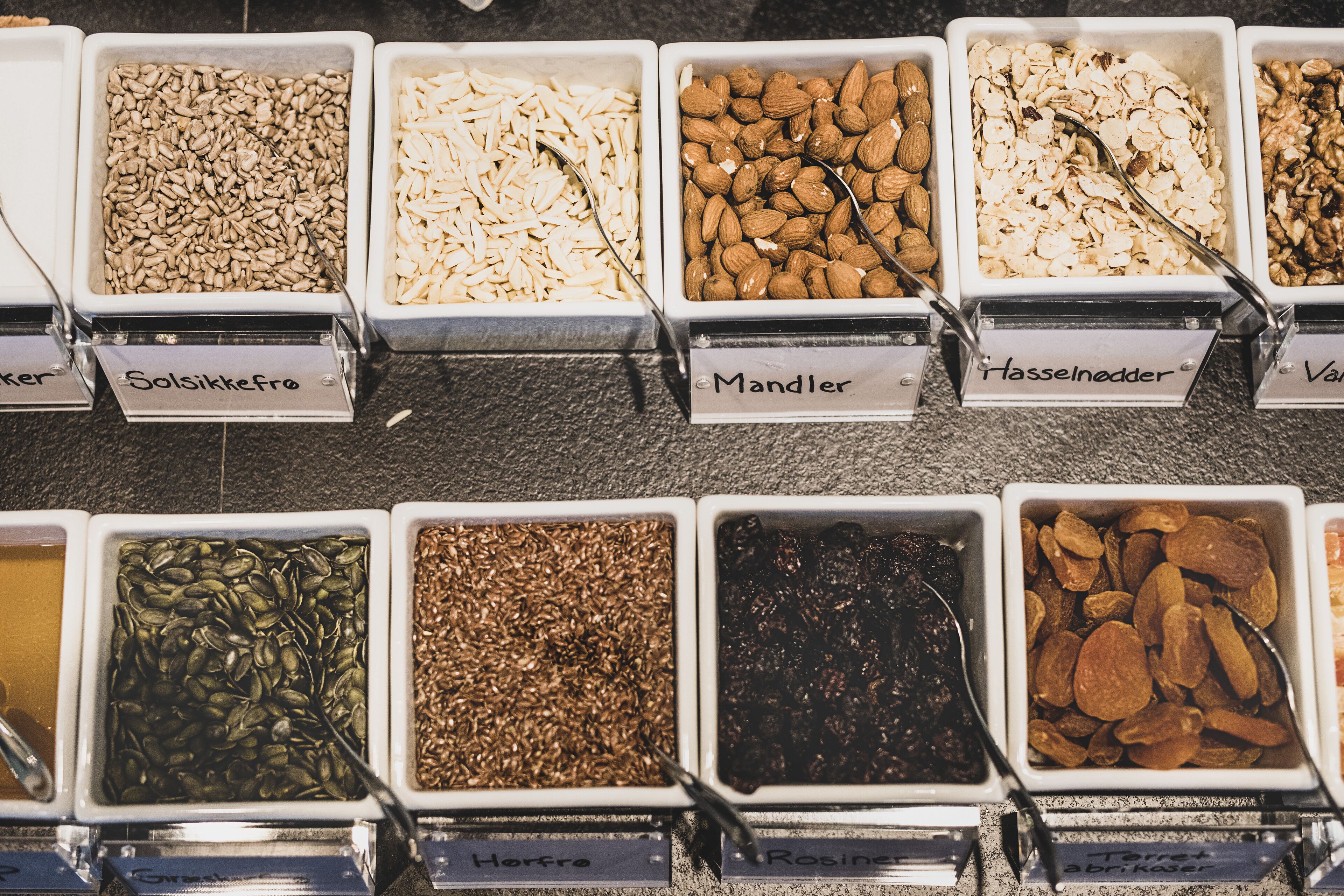 A variety of nuts and seeds in labeled containers.