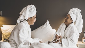 Two people in white bathrobes sitting on a bed with a bottle of wine and glasses. - Hotel Kolding (Kolding)