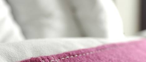 Primer plano de una cama con una manta rosa y almohadas blancas.