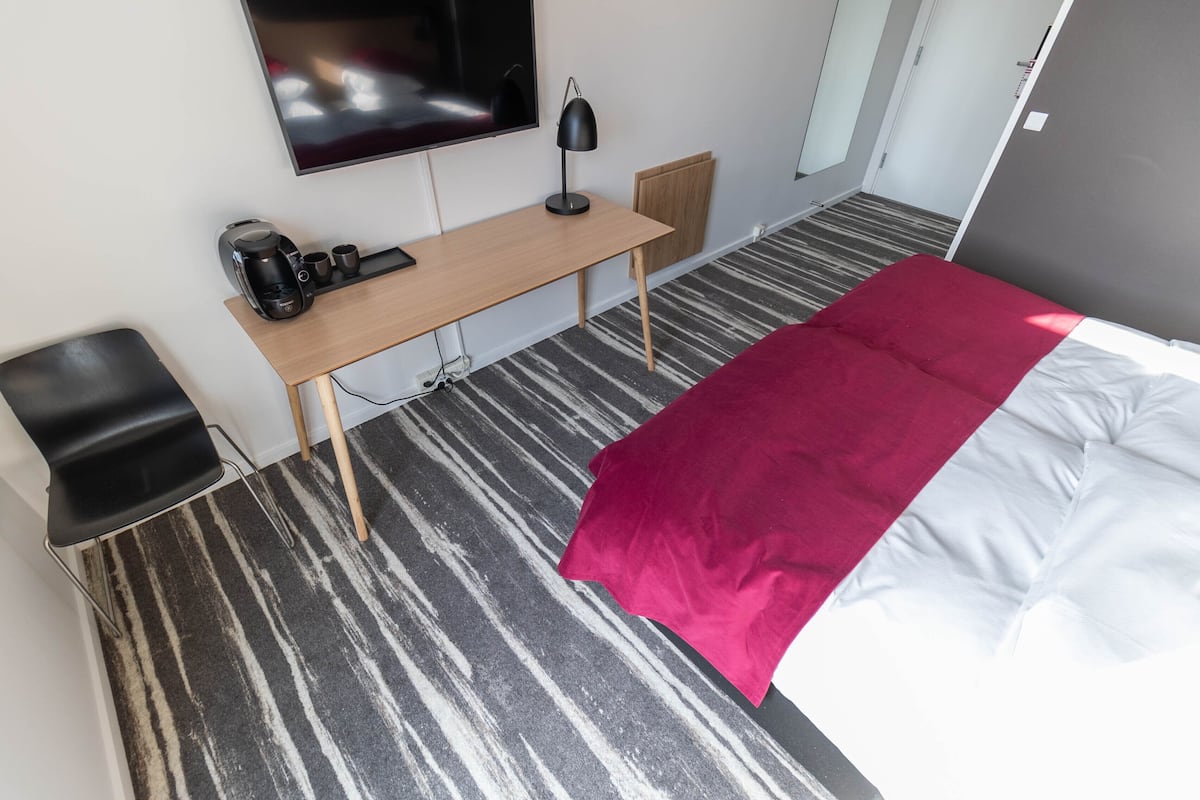 A hotel room with a bed, a desk with a computer, a chair, a TV, and a coffee maker.