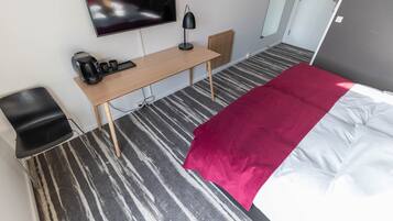Habitación de hotel con cama, escritorio con computadora, silla, televisor y cafetera.