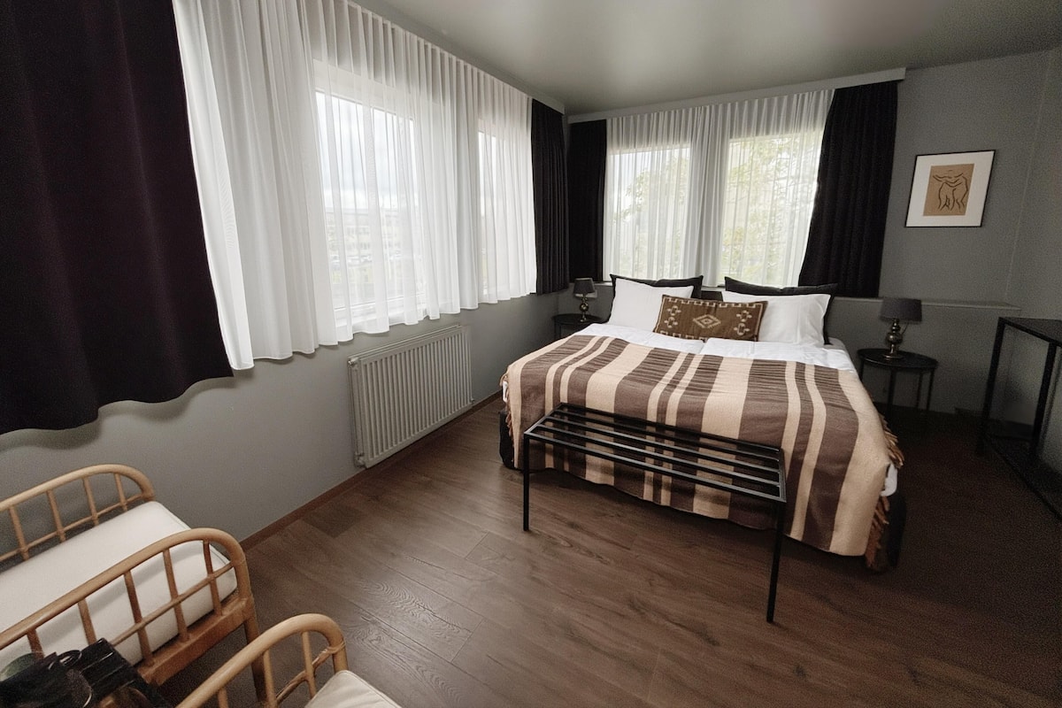Une chambre d’hôtel avec un lit, une chaise, une table et une fenêtre avec des rideaux.