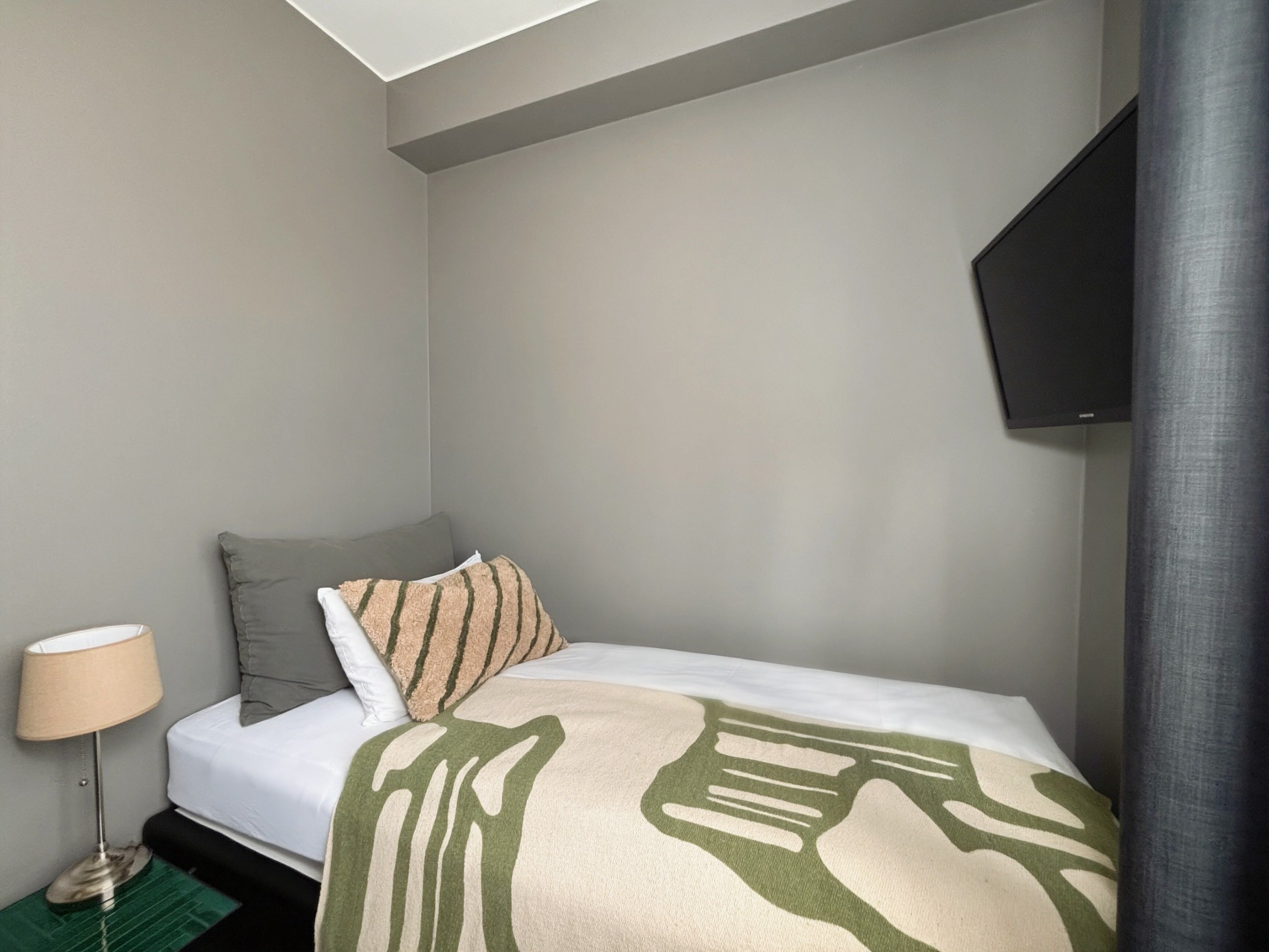A hotel room with a bed, a lamp, a TV, and a green rug.