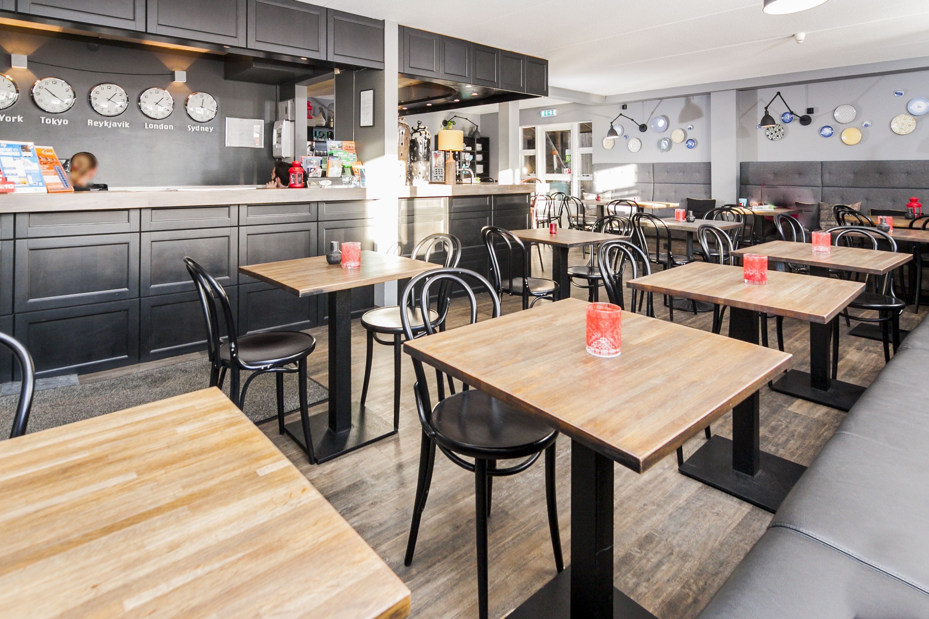 Ein Restaurant mit mehreren Tischen und Stühlen, einem Küchenbereich und Uhren, die Namen verschiedener Städte zeigen.