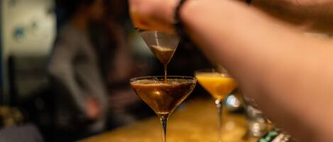 A martini glass on a bar with a smartphone and a bottle nearby.