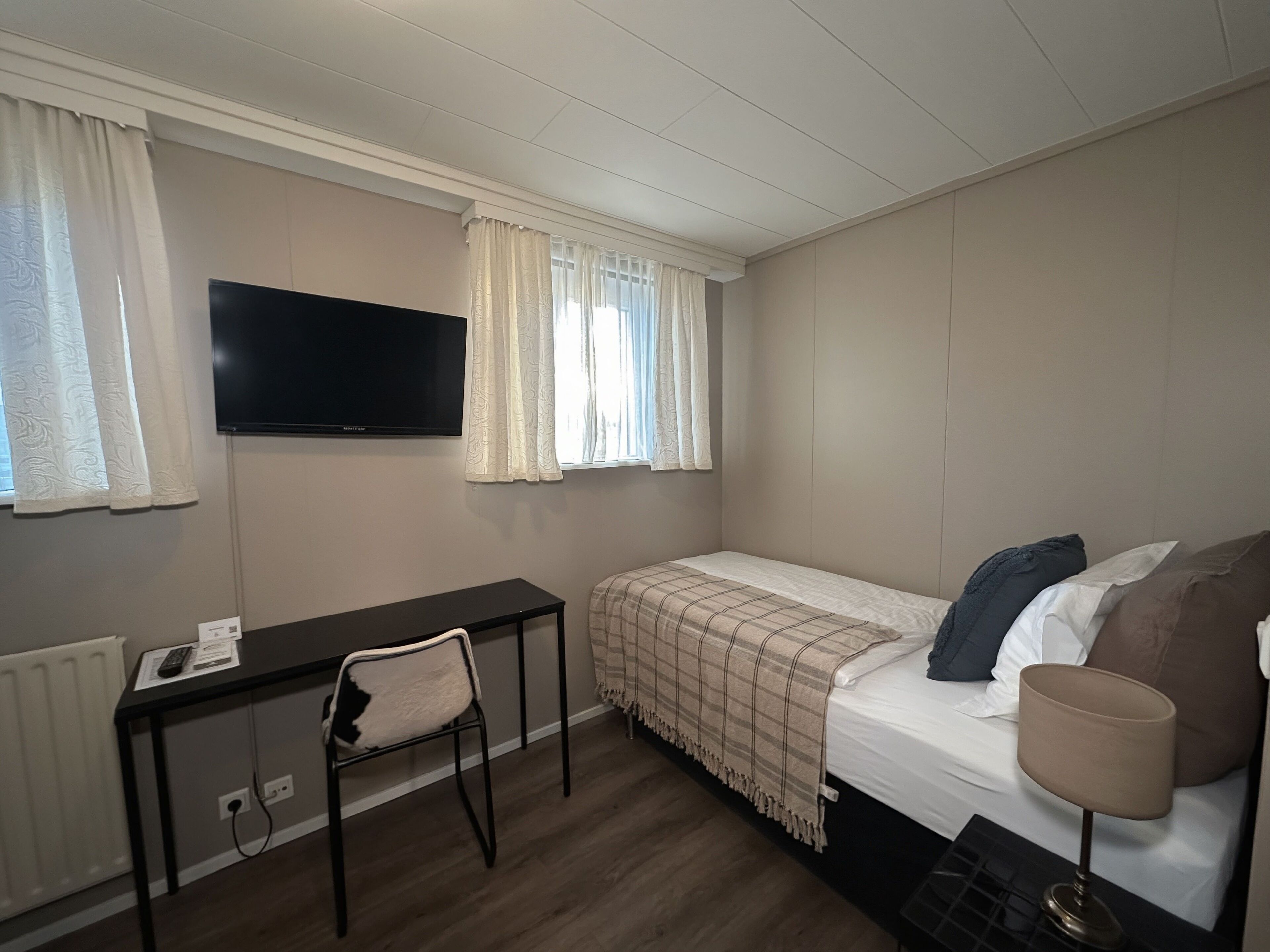 Una habitación pequeña y ordenada con cama, escritorio, silla y televisor.