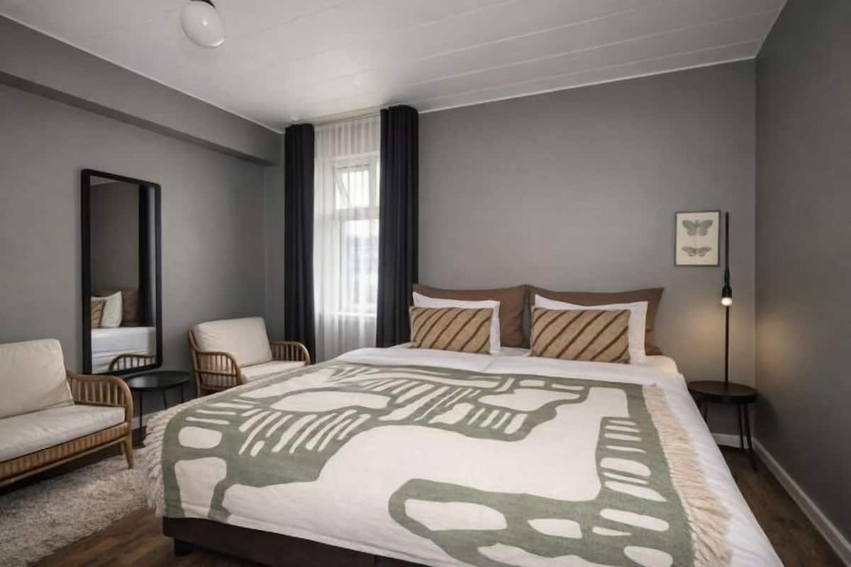 Une chambre à coucher comprenant un lit, deux chaises, un miroir, une table de chevet et un tableau accroché au mur.