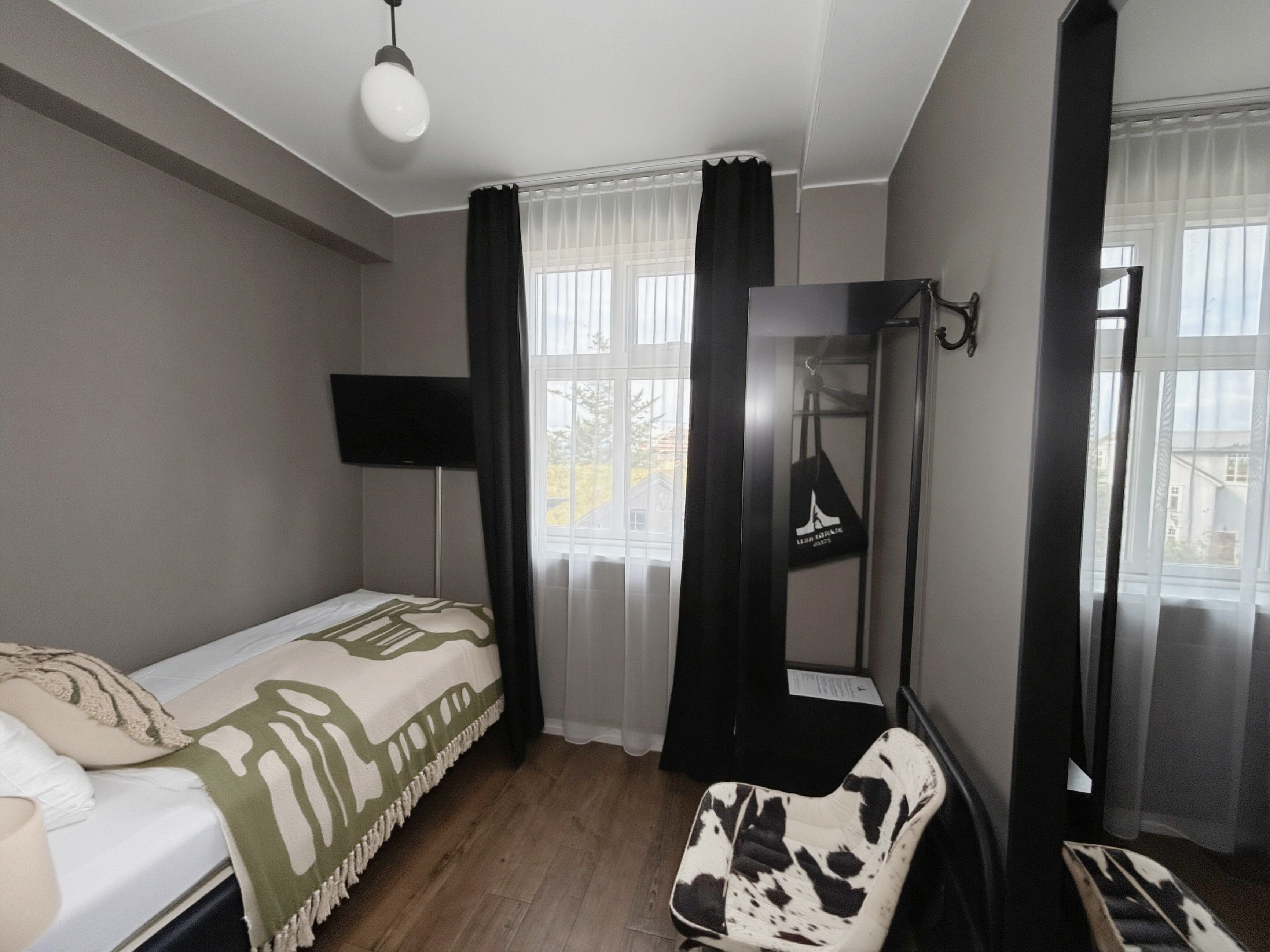 A hotel room with a bed, a chair, a TV, and a mirror.