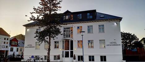 Un edificio blanco con el letrero HOTEL LEIFUR EIRIKSSON. Tiene varias ventanas, un balcón y un árbol en frente.