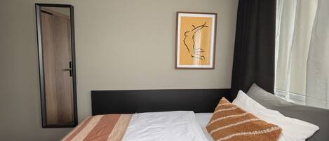 Habitación de hotel con cama, una obra de arte enmarcada en la pared, una puerta y una ventana con cortinas.