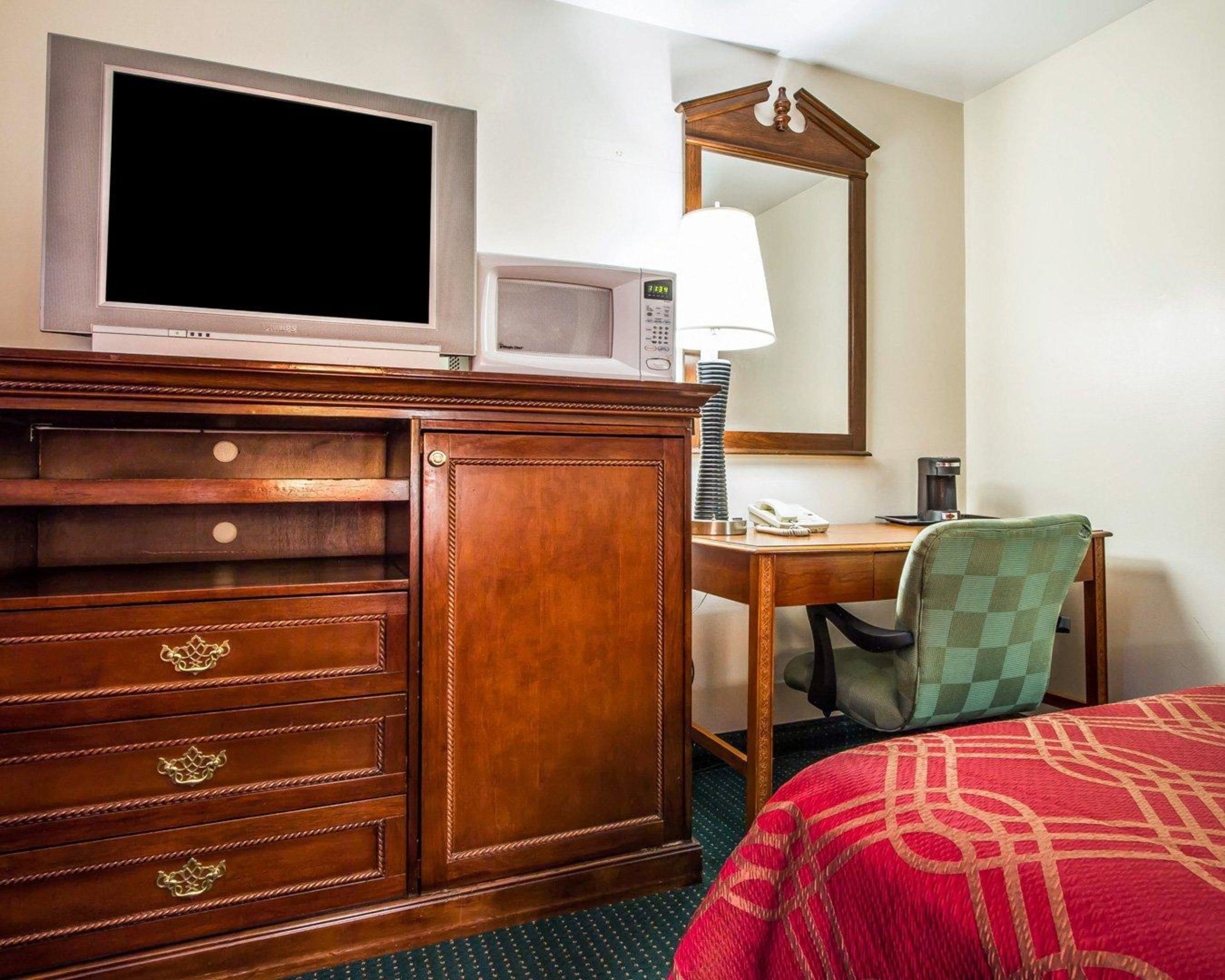 Habitación de hotel con cómoda de madera, escritorio con lámpara, teléfono y cama con manta roja.