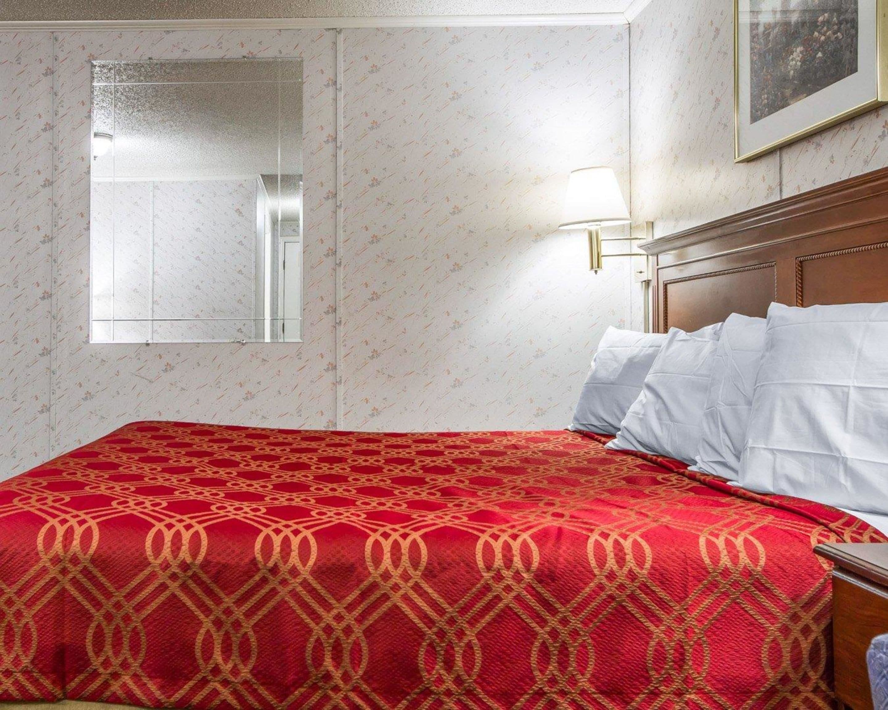 A hotel room with a bed, a window, and a wall-mounted lamp.