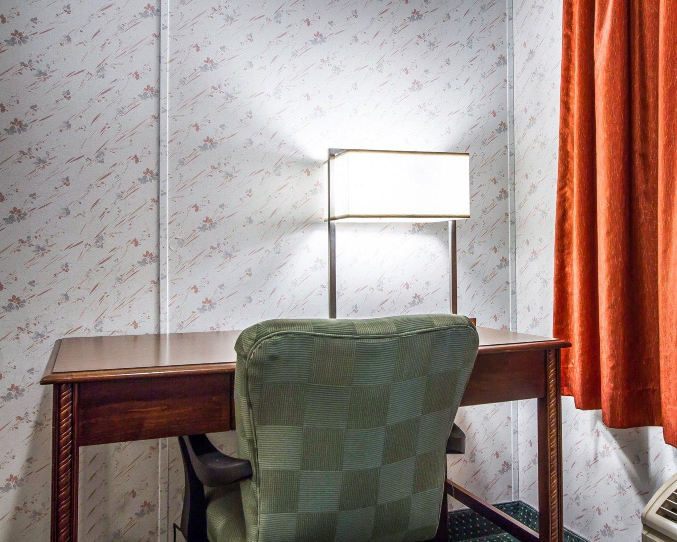 Un bureau d’angle avec un bureau en bois, une chaise verte, une lampe blanche et un papier peint à motifs floraux.