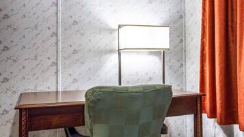 Un bureau d’angle avec un bureau en bois, une chaise verte, une lampe blanche et un papier peint à motifs floraux.