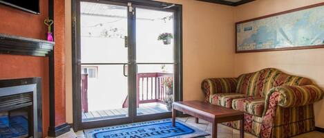 Una sala de estar con sofá, mesa de centro, chimenea y puerta corrediza de vidrio que da a un balcón con un felpudo que dice 'Welcome'.