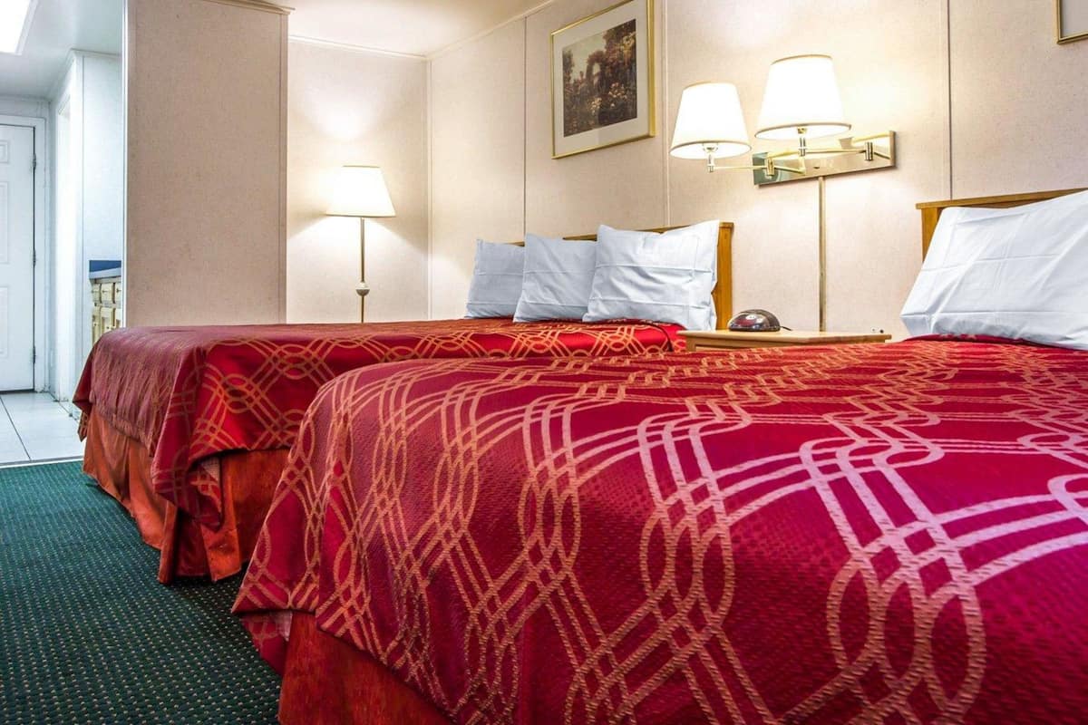 A hotel room with two beds, a large window, and a door leading to a balcony.