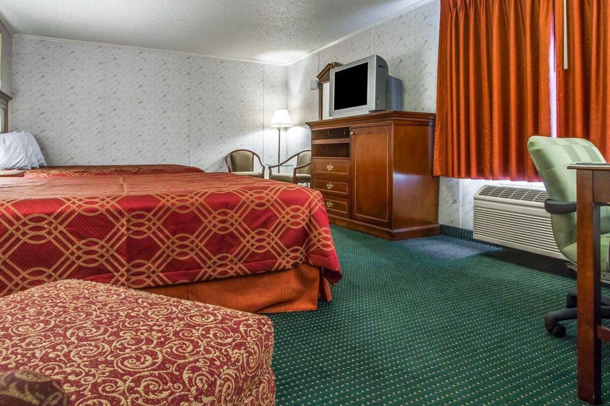 A hotel room with two beds, a desk, a television, and a window with curtains.