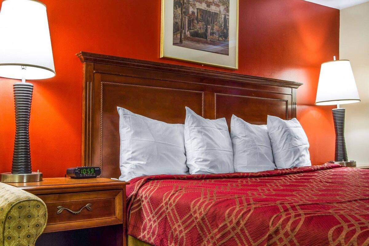 A hotel room with a wooden headboard, a red patterned bedspread, and two bedside lamps.
