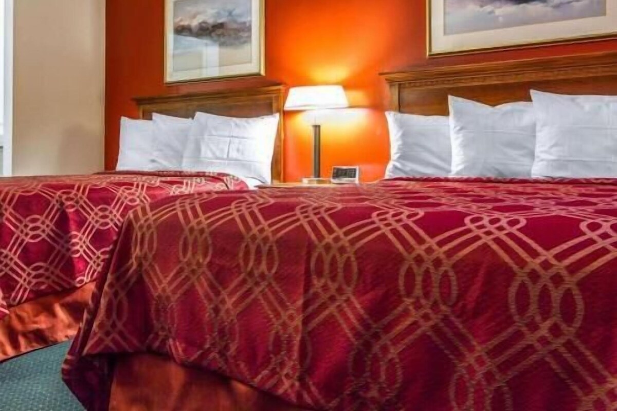 A hotel room with two beds, a nightstand with a lamp, and two framed pictures on the wall.