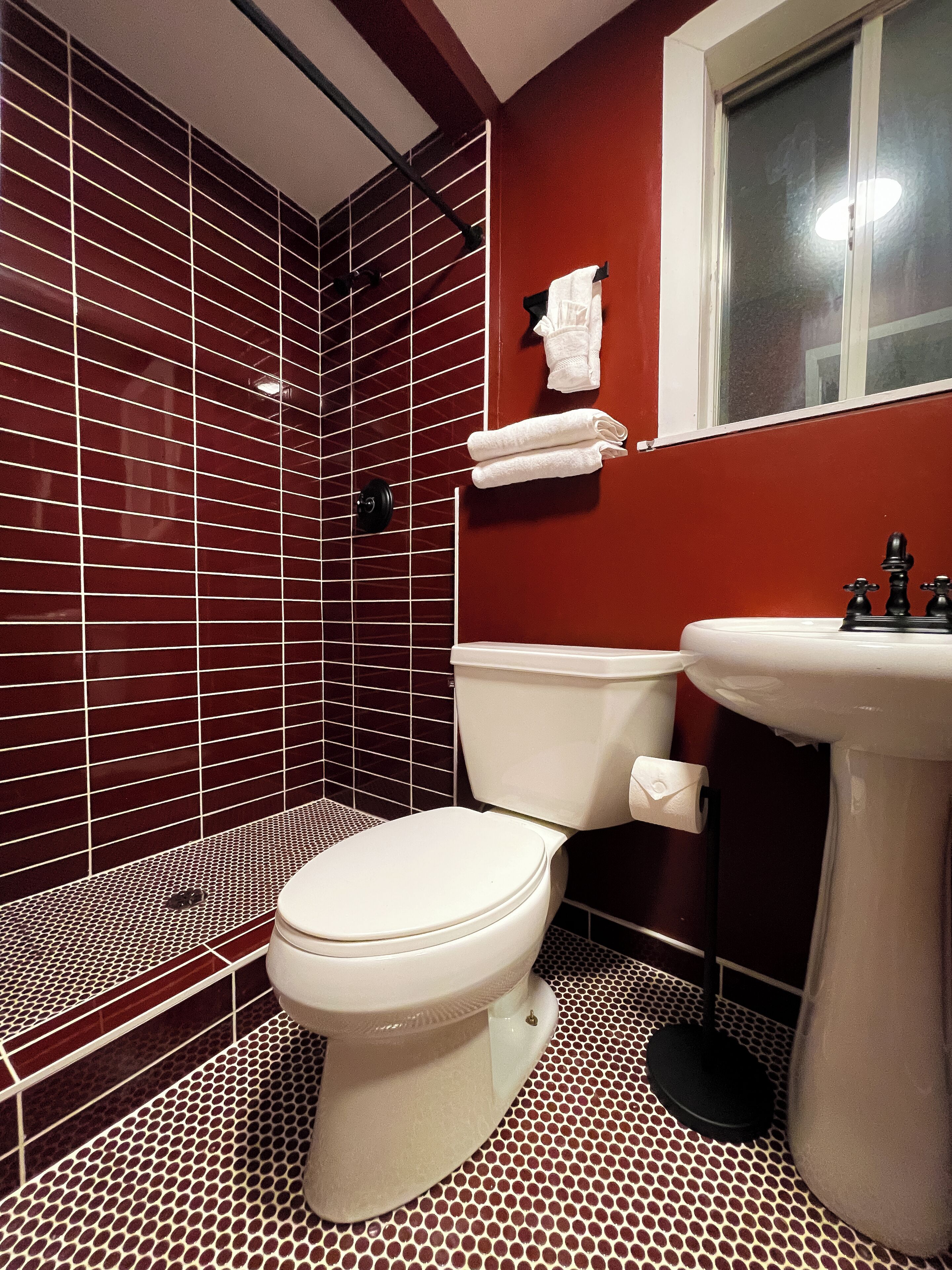 Une salle de bain avec des toilettes blanches, un lavabo et un espace douche dont les murs sont recouverts de carreaux rouges.