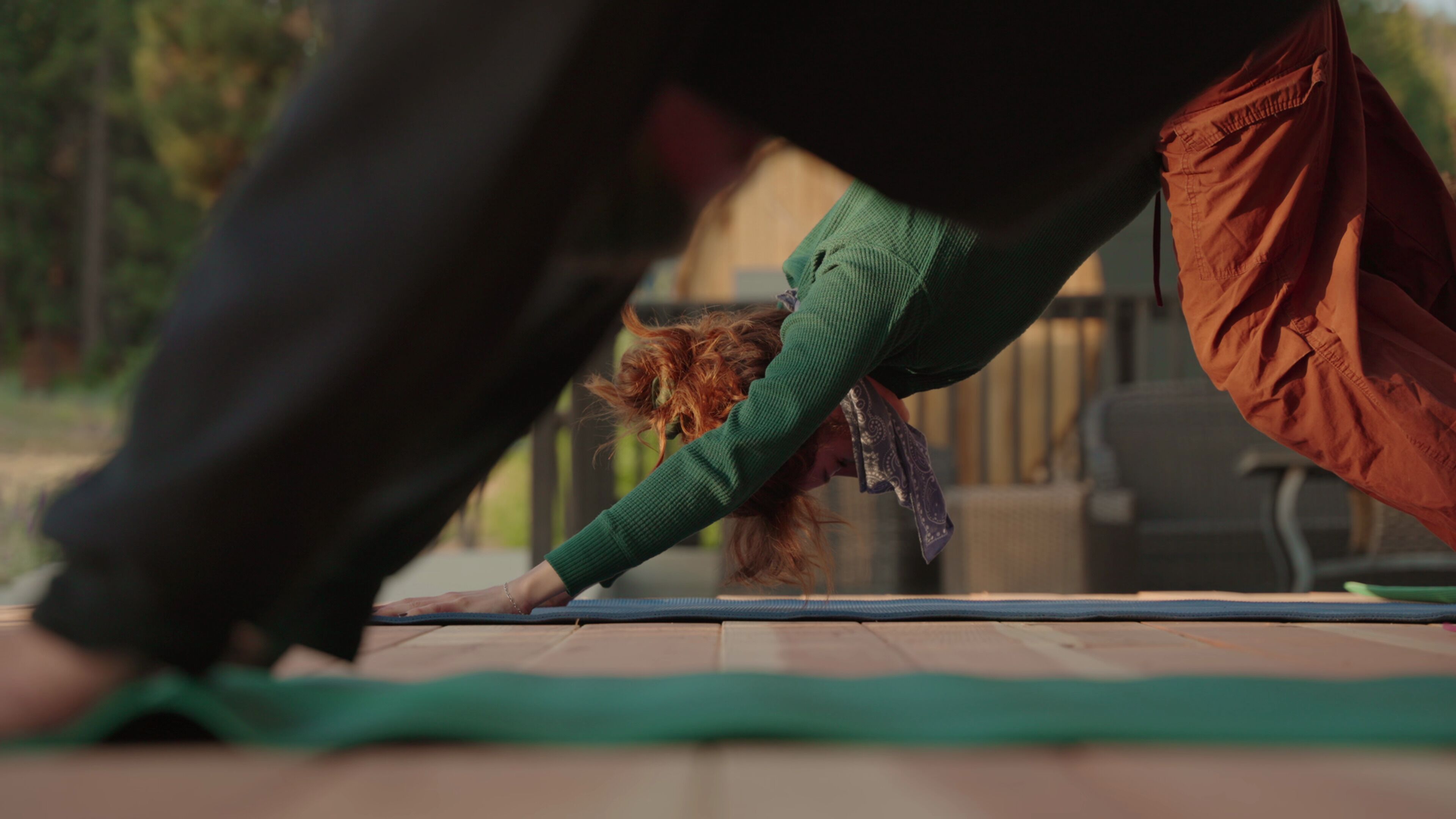 Een persoon in een groene trui en bruine broek doet een yoga-houding op een mat.