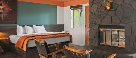 Une chambre à coucher avec un lit, une cheminée en pierre, une fenêtre et une œuvre d’art accrochée au mur.