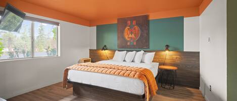 A modern bedroom with a large bed, two bedside lamps, a window, and a wall-mounted artwork.