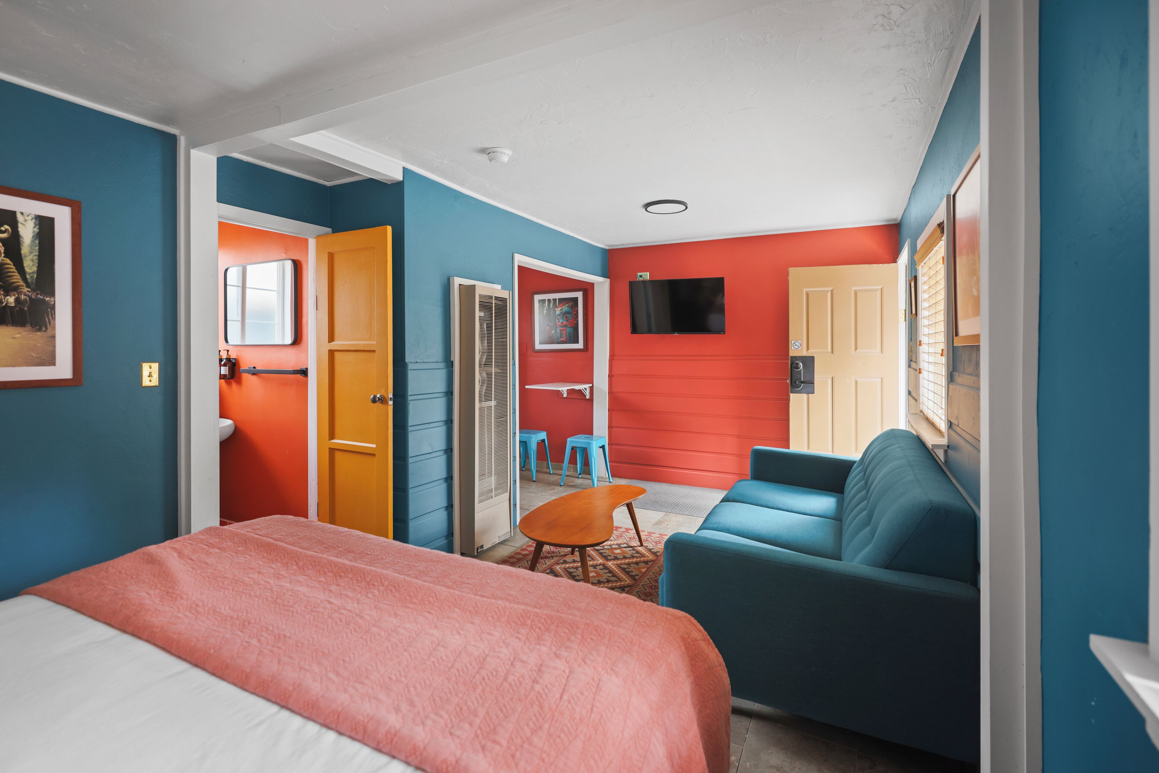 A hotel room with a bed, a blue sofa, a small table, and a TV mounted on the wall.