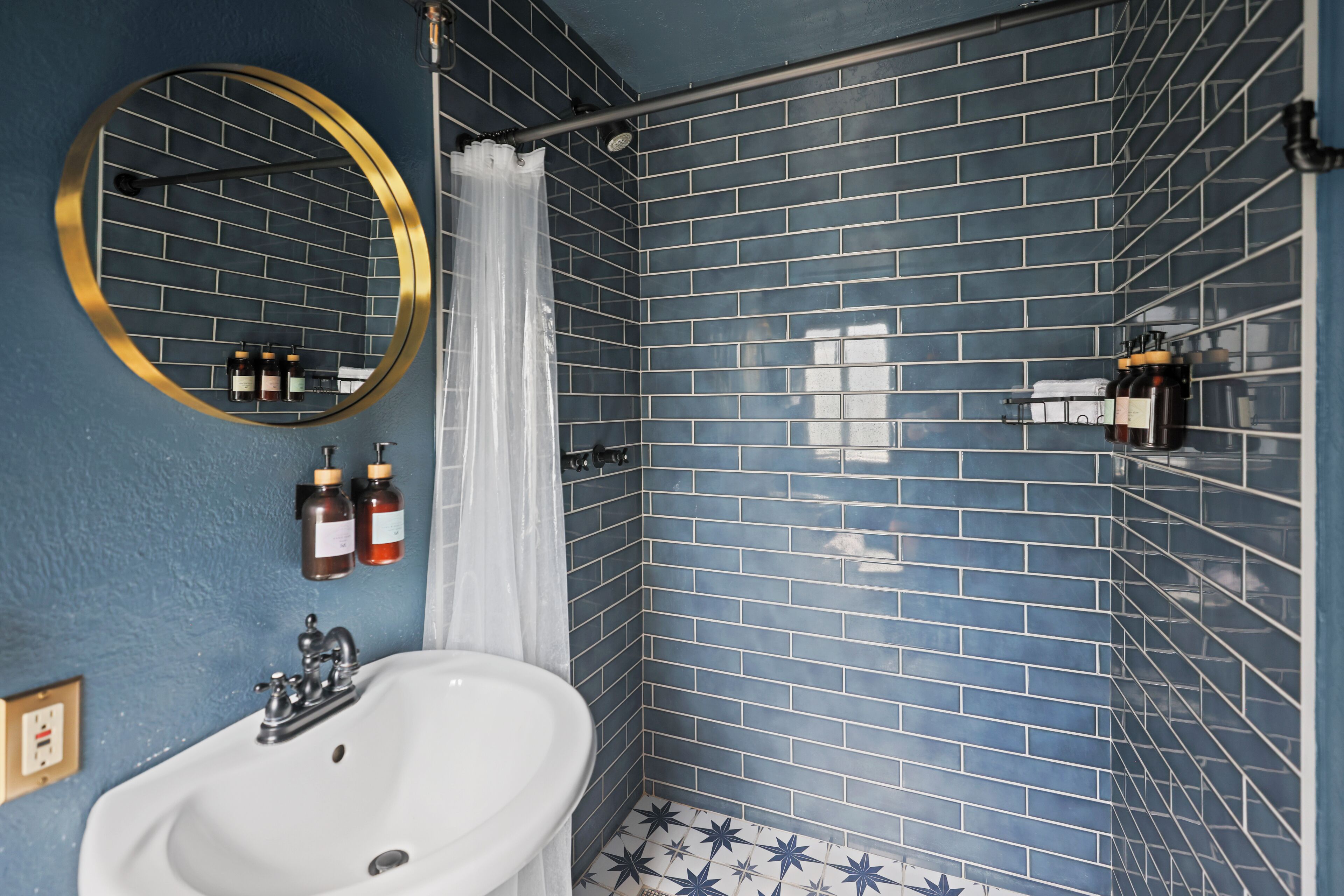 A bathroom with a white sink, a round mirror, and blue-tiled walls.