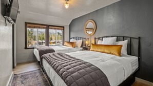 Quarto com duas camas, uma janela grande, um espelho redondo e um lustre.