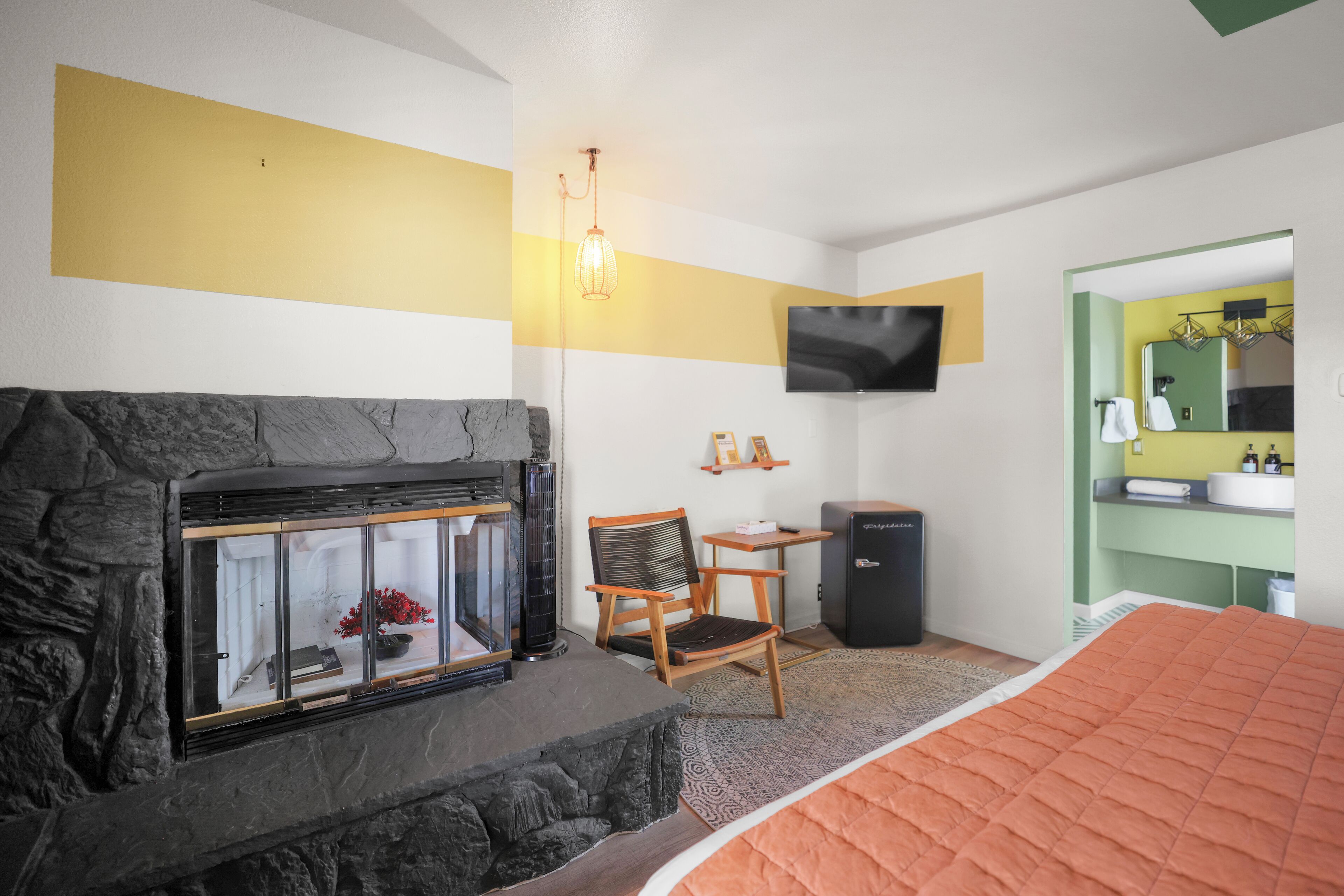 A bedroom with a fireplace, a bed, a desk, a chair, and a television.