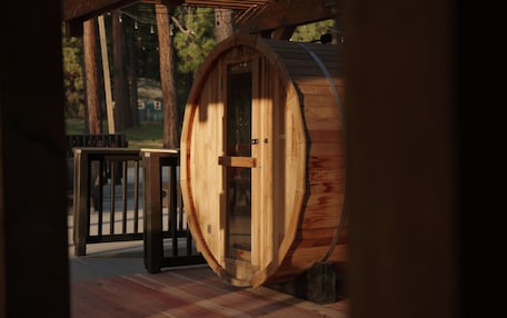 A wooden barrel-shaped structure with a glass door, a black metal railing, and a checkered floor.