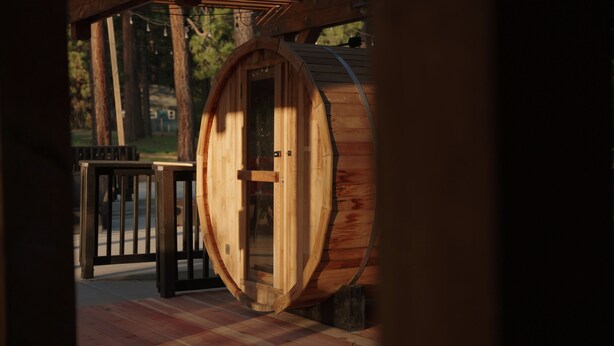Uma estrutura em forma de barril de madeira com porta de vidro, guarda-corpo de metal preto e chão xadrez.