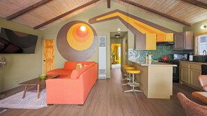 Um loft espaçoso com pé direito alto, um sofá laranja aconchegante, uma cozinha com armários amarelos e um espaço de jantar com banquetas.