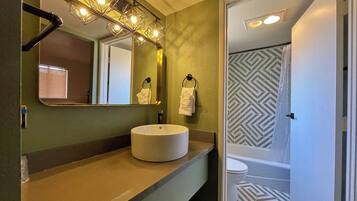 A bathroom with a vanity, a sink, a mirror, and a shower area.