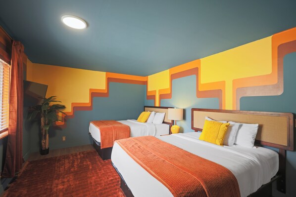 A hotel room with two beds, a large potted plant, and a patterned rug.