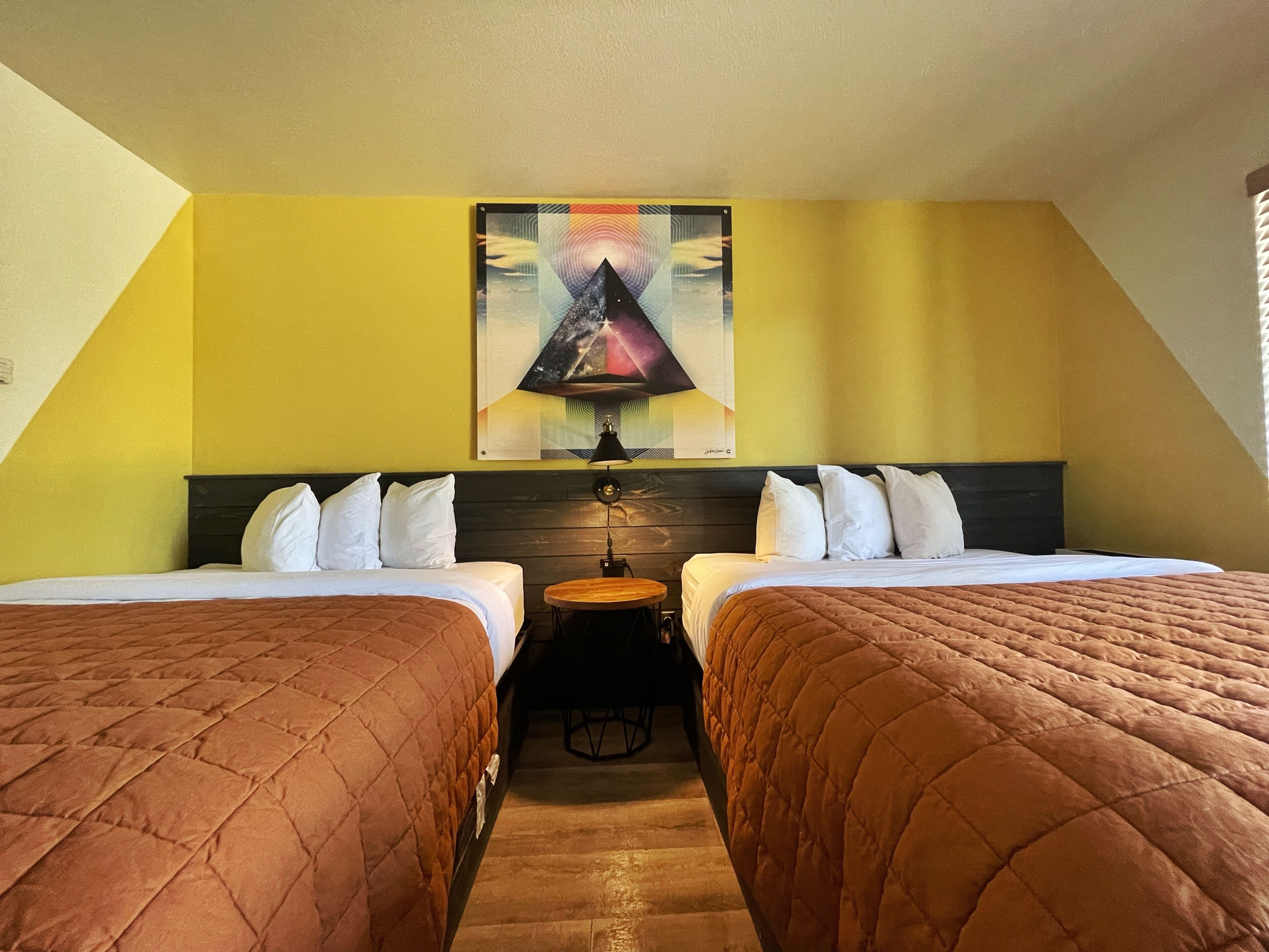A hotel room with two beds, a small table, and a painting on the wall.