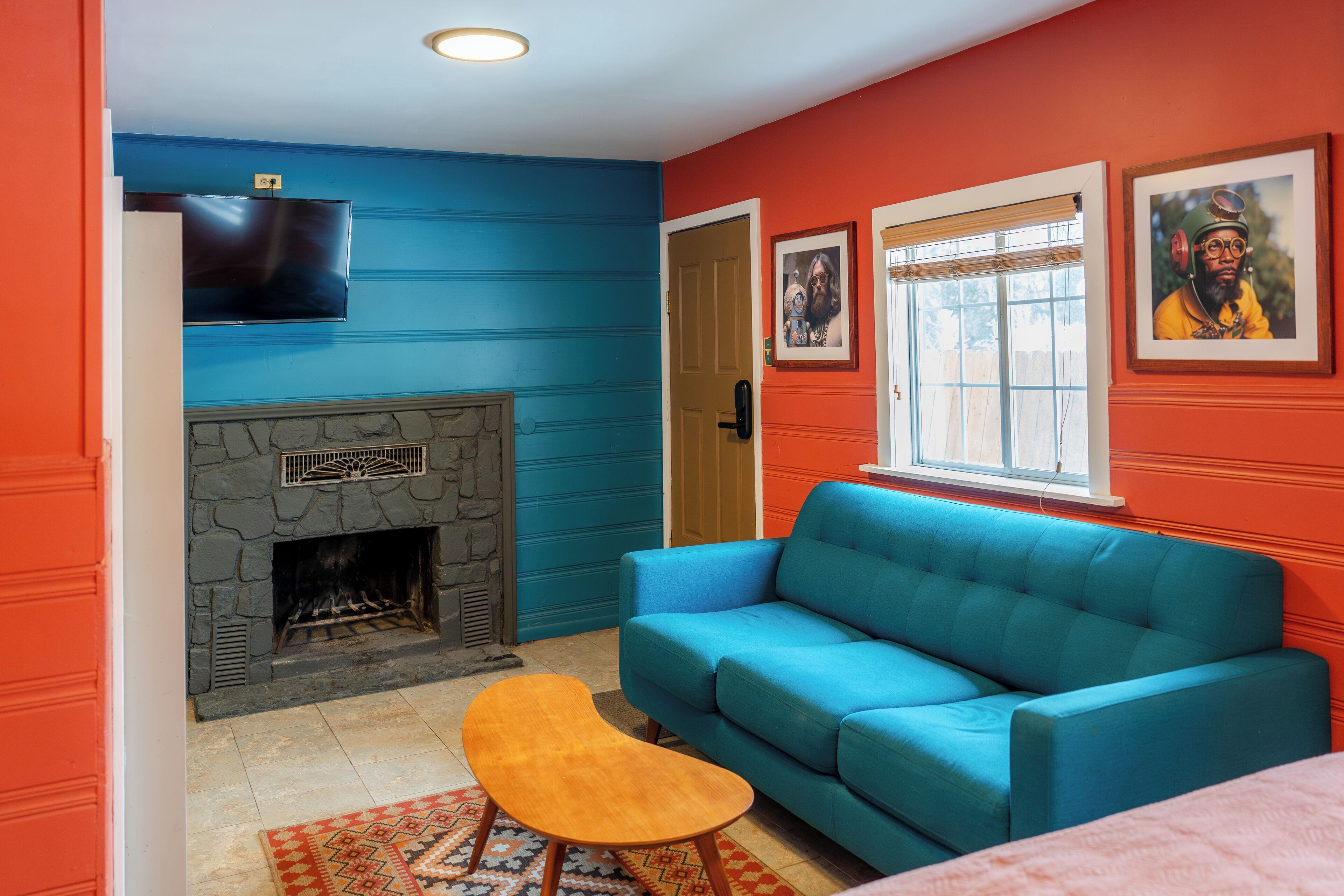 A living room with a stone fireplace, a blue sofa, and a television mounted on the wall.