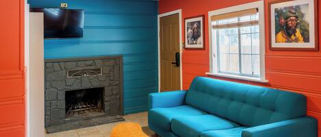 A living room with a stone fireplace, a blue sofa, and a television mounted on the wall.