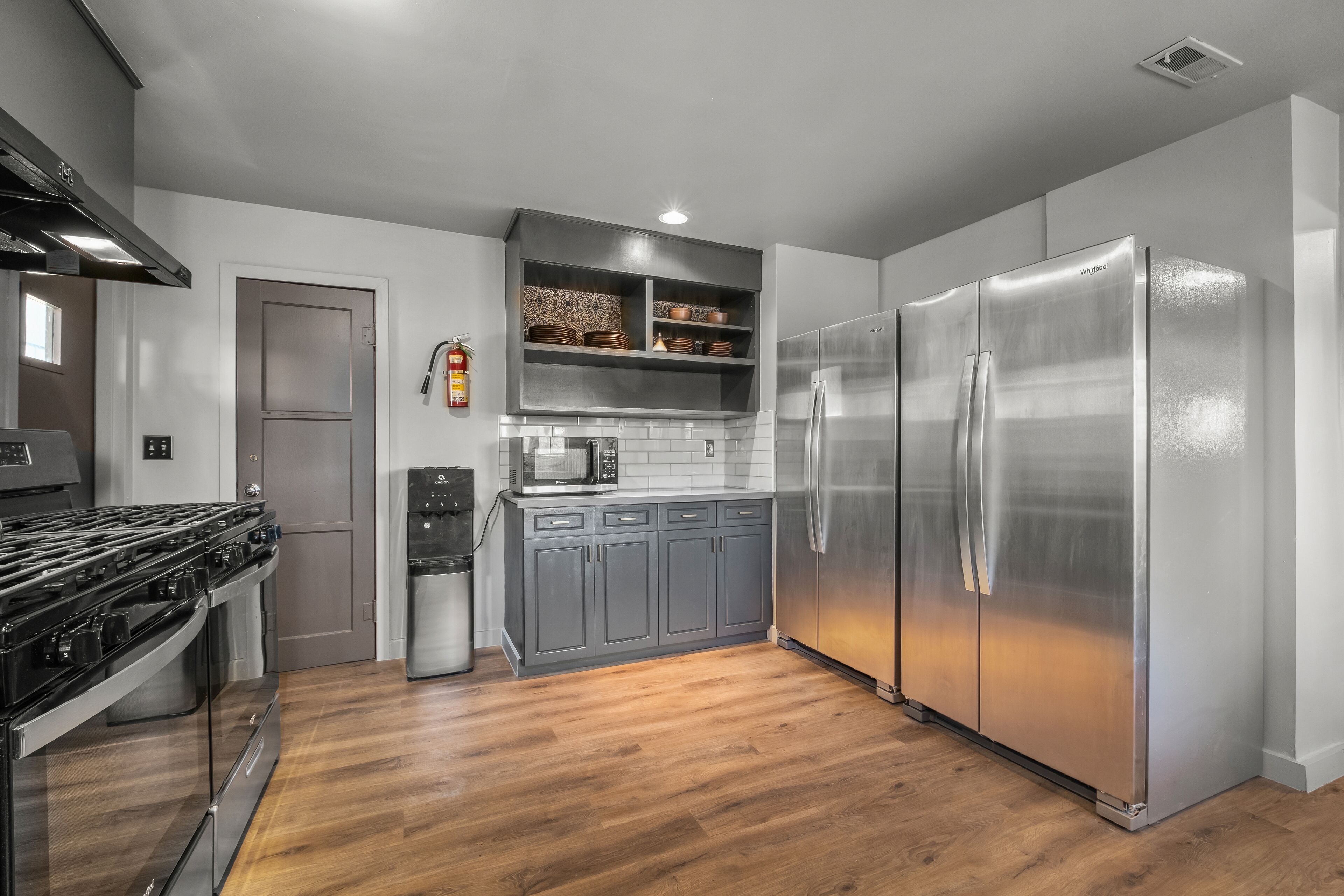 Een moderne keuken met roestvrijstalen apparatuur, grijze kastjes en een houten vloer.