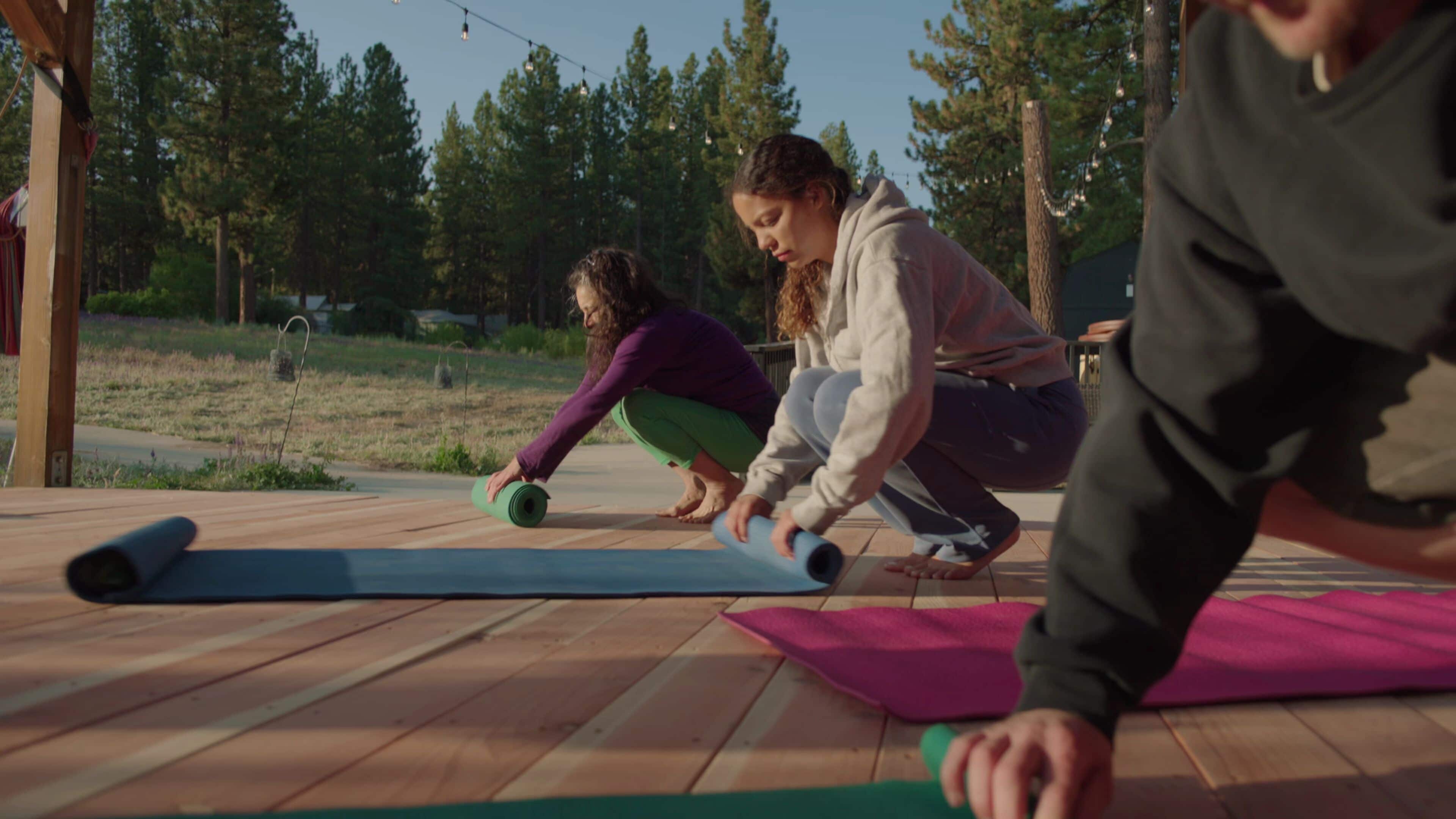 A wooden deck with yoga mats and a person in a purple top.